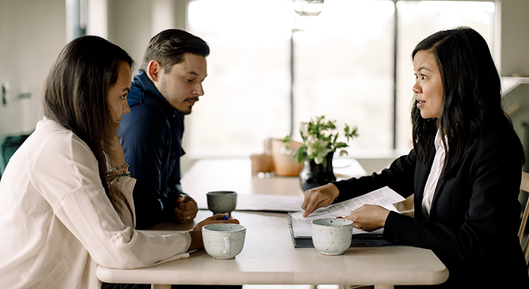 Customers discussing property documents with saleswoman at table in new house