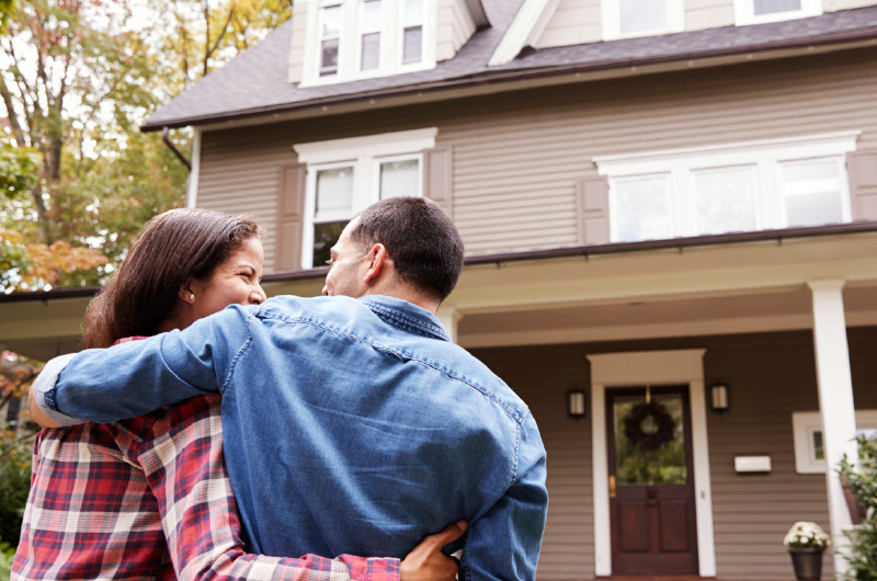 Couple hugging outside of front of house